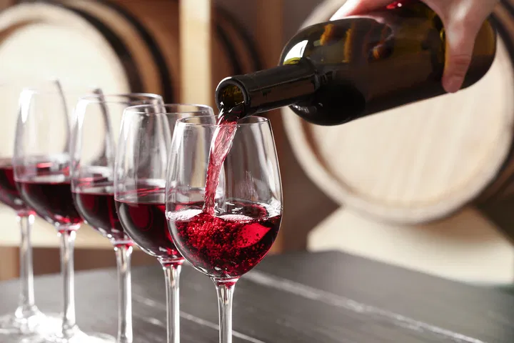 Five red wine glasses being filled by a pouring wine bottle.
